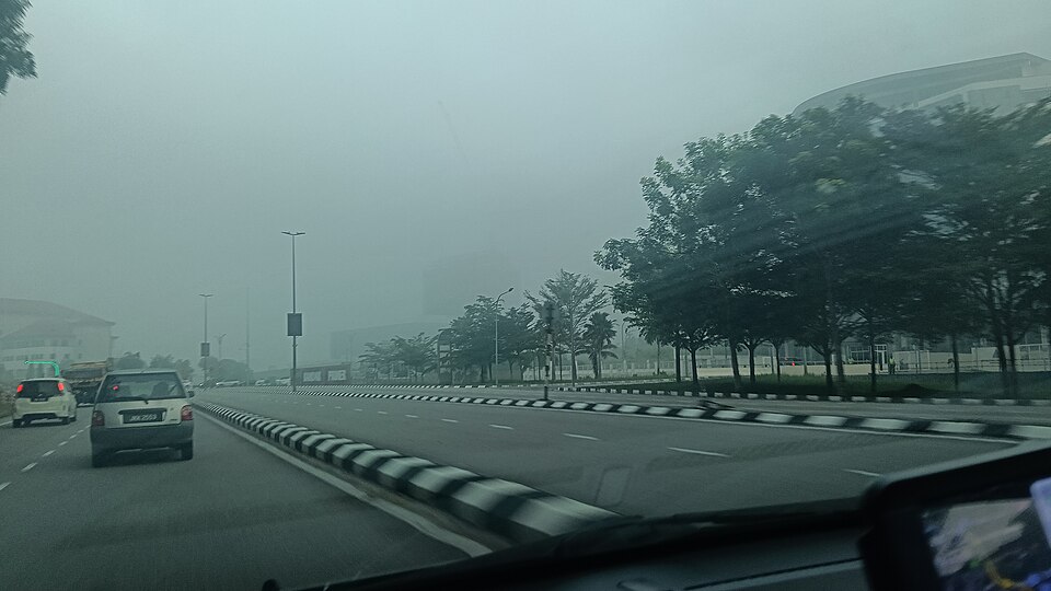 Pemandangan dari dalam kereta di sebuah jalan raya di Kluang, Johor, kereta di hadapan dan pokok di tepi jalan kelihatan kabur dalam jerebu kelabu tebal