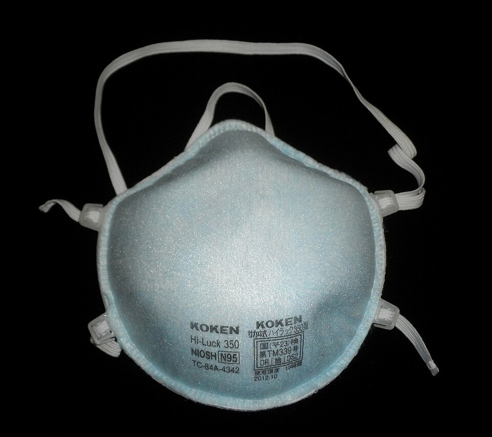 Sebuah pelitup respirator N95 putih dengan tali elastik, diletakkan di atas permukaan rata